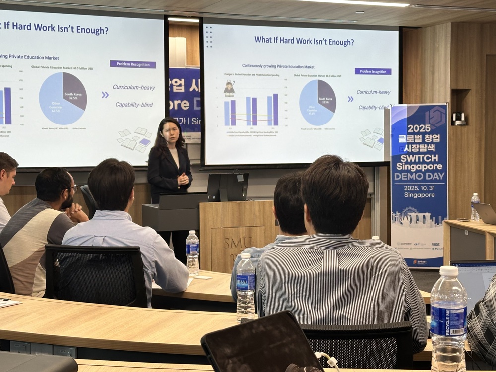 A D.Company presenter pitching to a seated audience at the SWITCH Singapore Demo Day, with a slide titled &lsquo;What If Hard Work Isn&rsquo;t Enough?&rsquo; on the screens behind her.